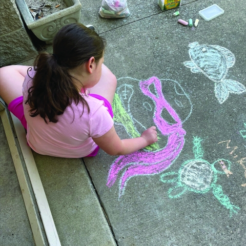 Photo of a girl drawing on a sidewalk with chalk
