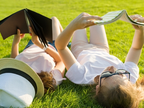 Two teen girls lying on their backs in the grass reading books