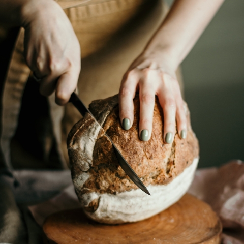 a woman's hands cutting a loaf of sourdough bread