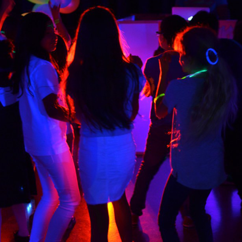 a group of teens with their back to the camera in a low-lit room. They are wearing glow bracelets.