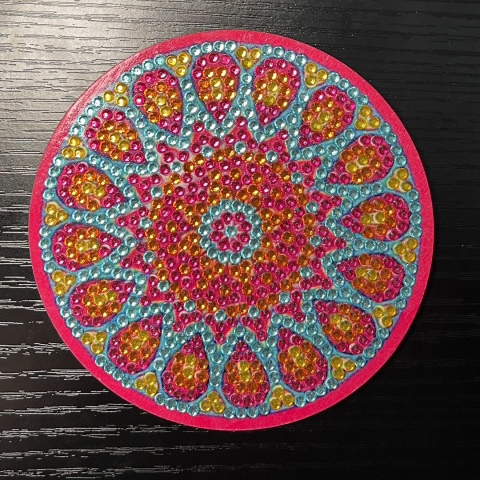 a round coaster with a pattern created by pink, yellow, and blue beads