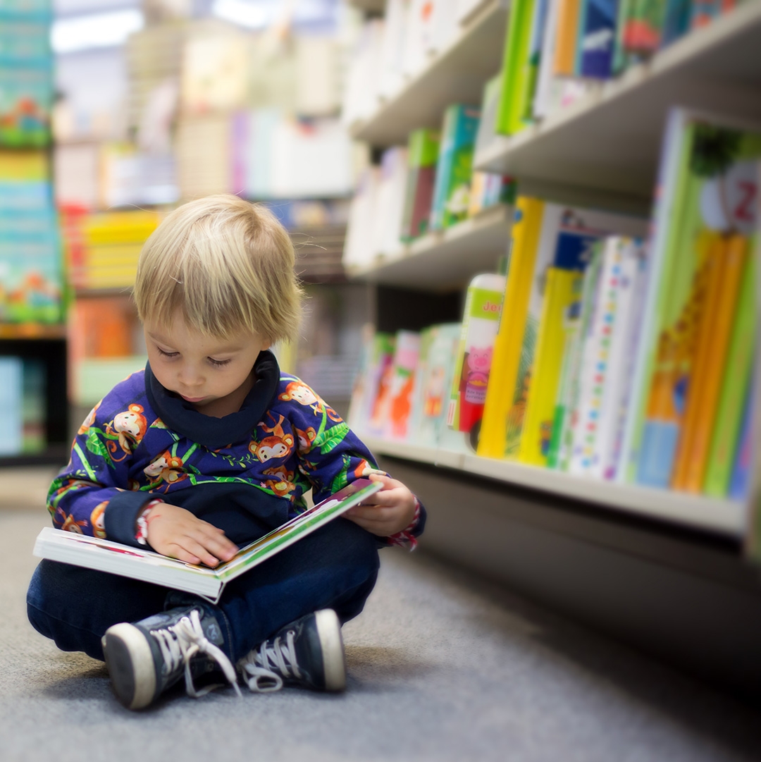 Child sitting in the floor of a library, looking at a book